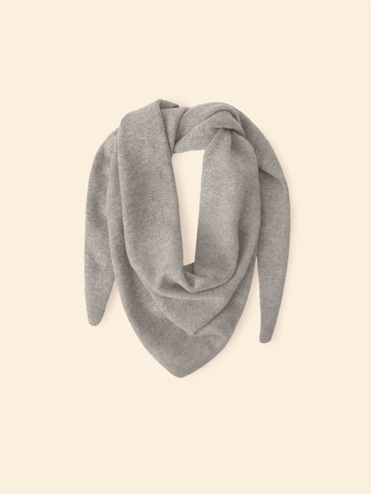 Le Petit Scarf—a light gray cashmere scarf with pointed ends, made in Los Angeles—is displayed in a loose triangular shape on a plain beige background.