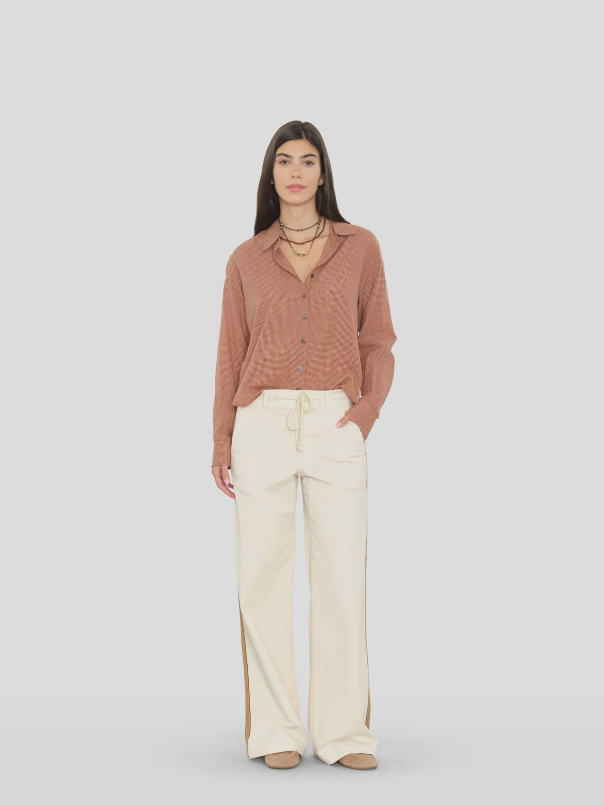 Xirena Bradshaw Pant styled with a brown button-up shirt and tan shoes, set against a light gray background.