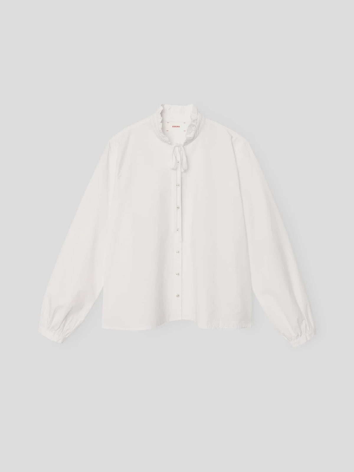 White blouse with ruffled neck, front buttons, and bow by Xirena; Tatiana Shirt in poplin, shown on plain background.