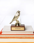 A JE Trophy on a base with the inscription "YOU'RE SO FLY," placed atop a stack of colorful hardcover books against a white background, adds unique style to any decor.